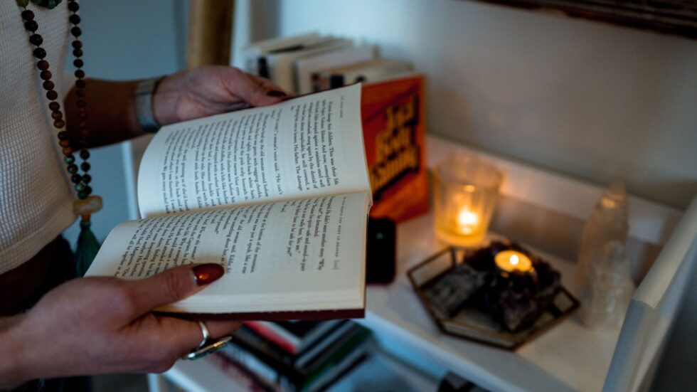 Una donna legge un libro aperto a lume di candela in un'atmosfera calda e raccolta