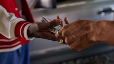 Due mani si scambiano un fascio di banconote all'aperto vicino a un'auto