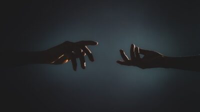 Silhouette di due mani che si protendono l'una verso l'altra in un ambiente buio