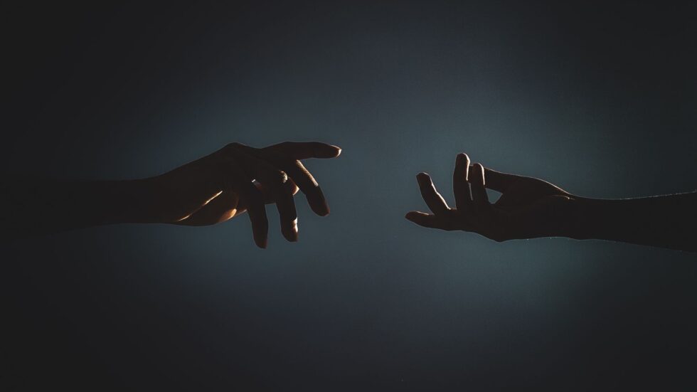 Silhouette di due mani che si protendono l'una verso l'altra in un ambiente buio