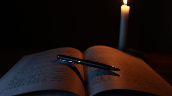 Libro aperto e penna su una scrivania illuminata da una candela, atmosfera raccolta per la lettura.