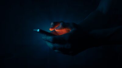 Mani che tengono uno smartphone al buio, illuminate dal bagliore dello schermo