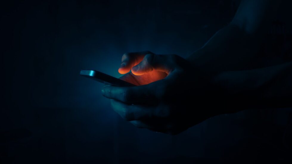 Mani che tengono uno smartphone al buio, illuminate dal bagliore dello schermo