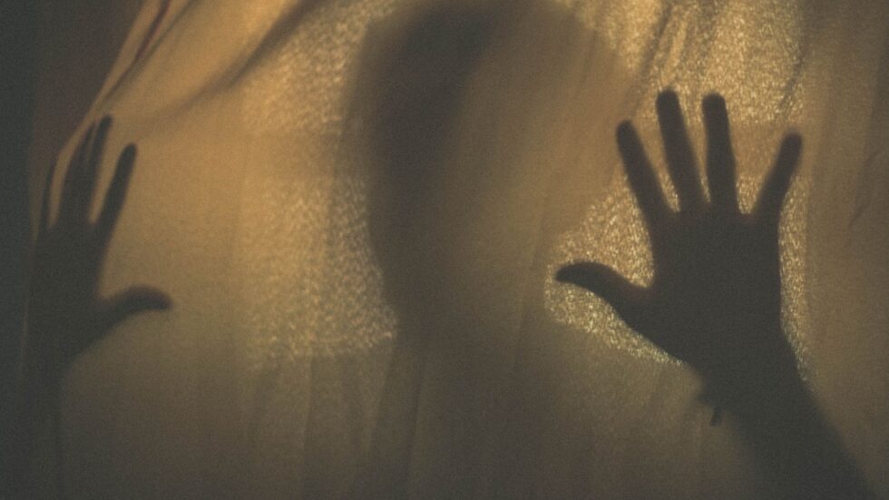 Silhouette di mani premute contro una tenda di tessuto, con ombra suggestiva