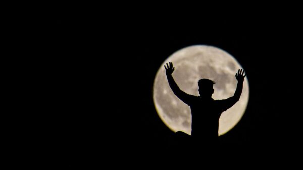 Silhouette di una persona con le mani alzate davanti alla luna piena