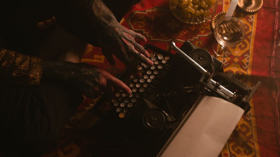 Mani tatuate digitano su una macchina da scrivere vintage tra candele accese e grappoli d'uva