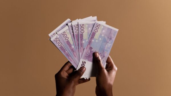 Mani che tengono diverse banconote da 500 euro su sfondo beige neutro
