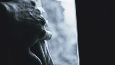 Mano che stringe una tenda con luce drammatica e ombre marcate in bianco e nero
