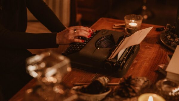 Mani digitano su una macchina da scrivere vintage in un'atmosfera calda illuminata da candele
