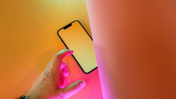 Una mano si protende verso uno smartphone su uno sfondo colorato giallo e rosa