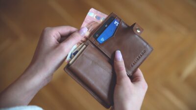 Mani che tengono un portafoglio in pelle con contanti e una carta di credito