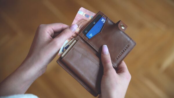 Mani che tengono un portafoglio in pelle con contanti e una carta di credito