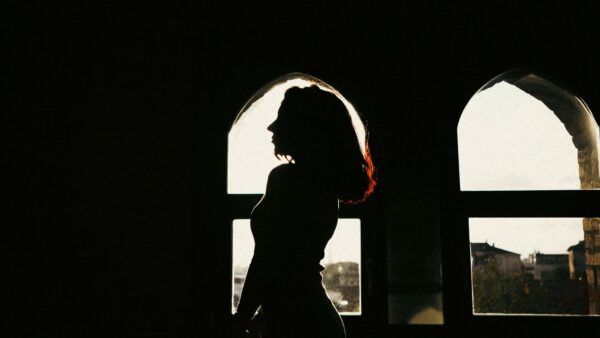 Silhouette di una donna in piedi accanto a una finestra ad arco, con un'ombra drammatica sulla parete