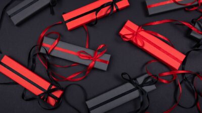 Scatole regalo rosse e nere con nastri decorativi disposte su una superficie nera