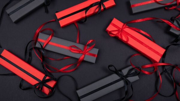 Scatole regalo rosse e nere con nastri decorativi disposte su una superficie nera